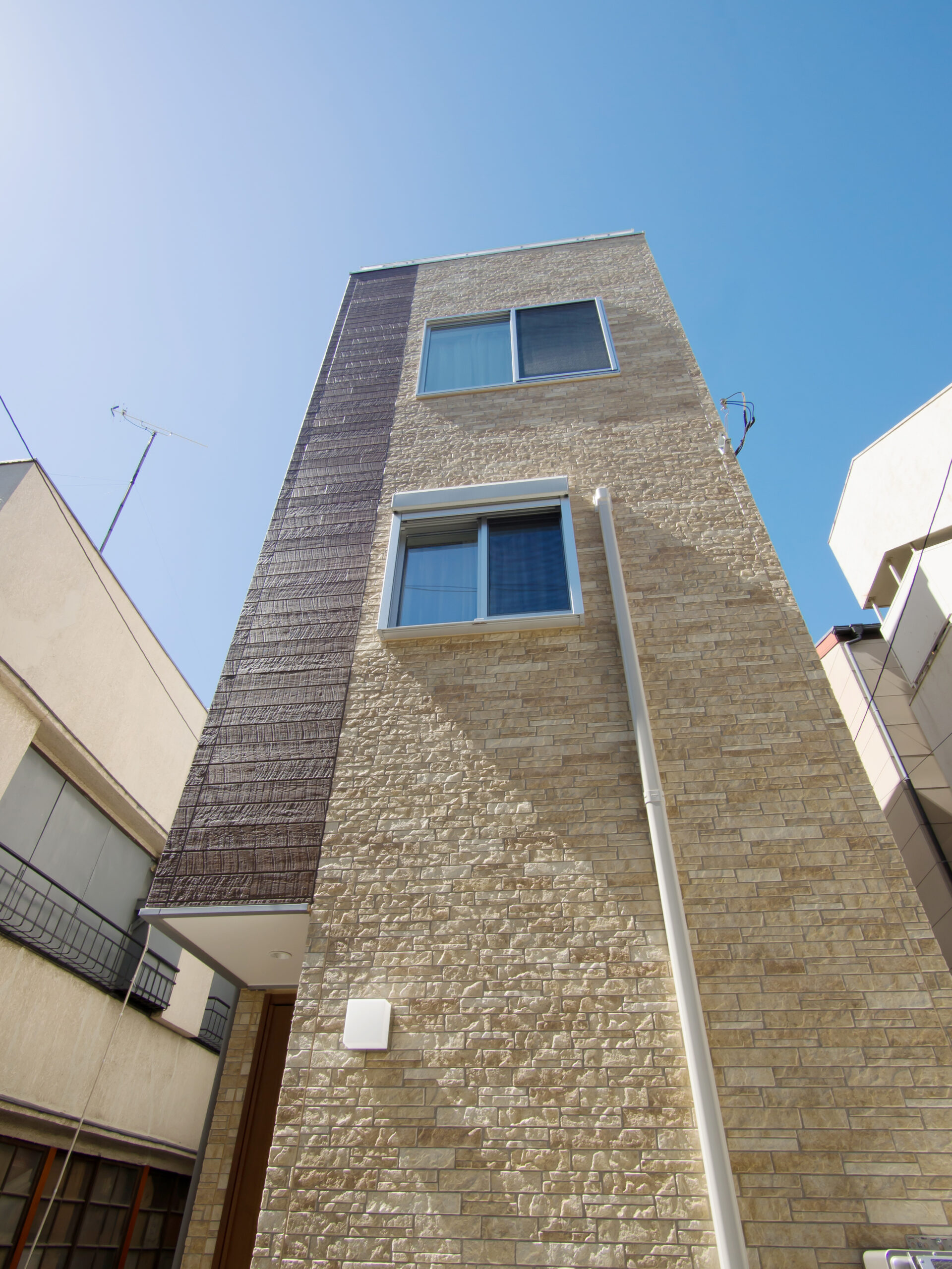 隣家に挟まれた間口の狭い3階建て住宅を見上げた外観